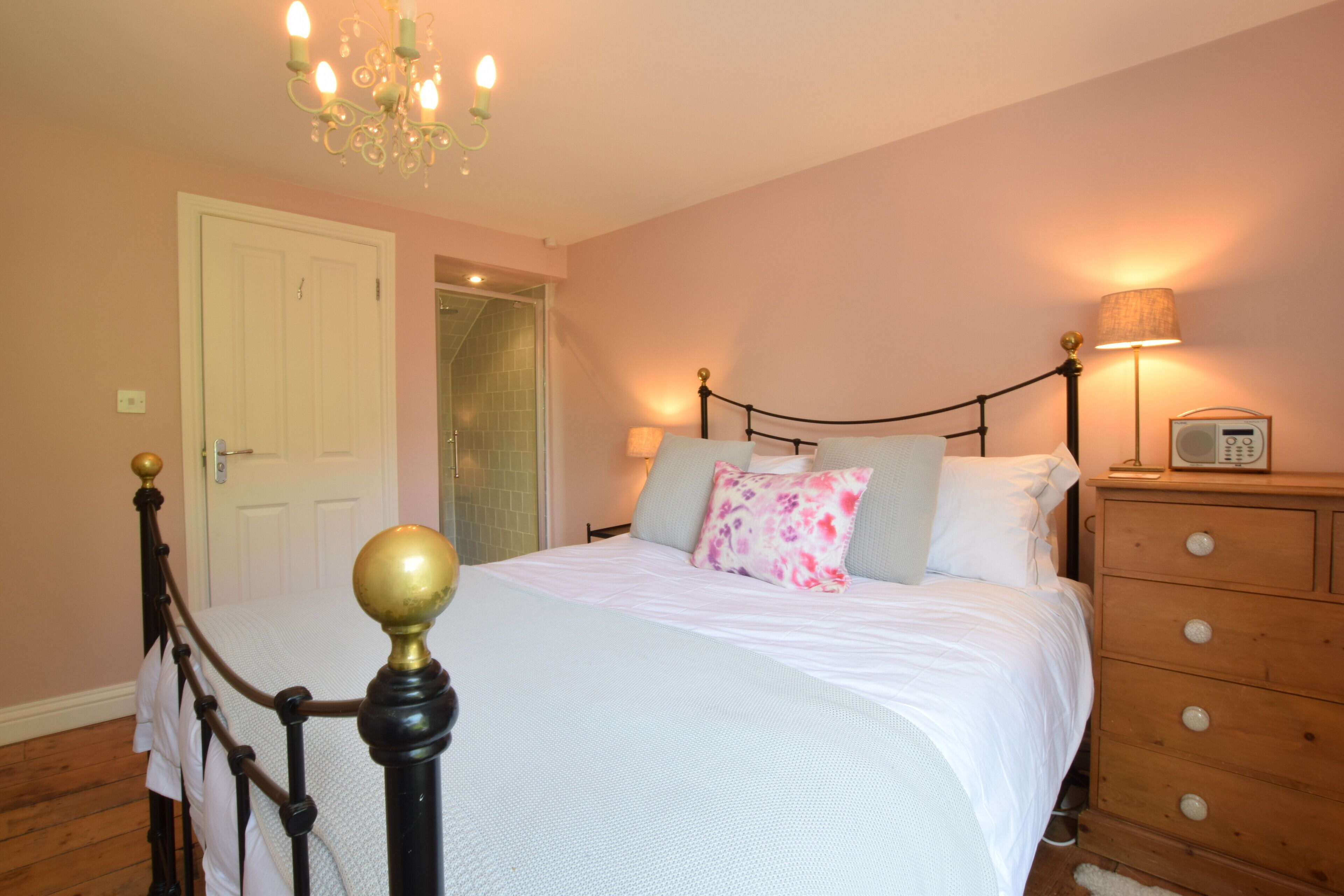 Quarto com cama, luminárias de cabeceira, cômoda e lustre.