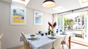 A dining area with a table set for two, featuring a blue tablecloth, white chairs, and a vase with flowers. - 15 Victoria Street, Southwold (Reydon)