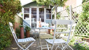 A garden patio with white metal chairs and a table, surrounded by potted plants and a wooden fence. - 15 Victoria Street, Southwold (Reydon)
