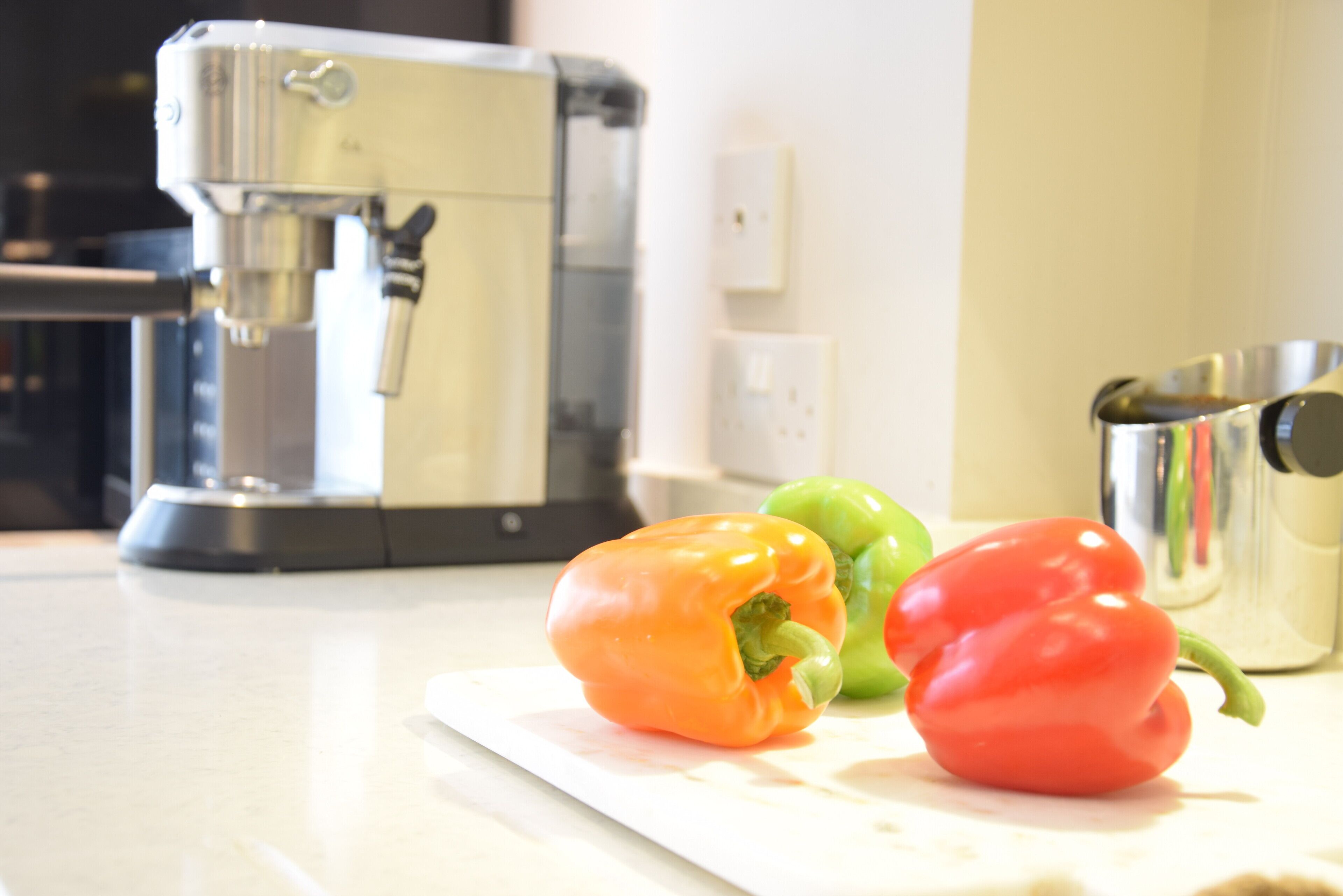 A kitchen counter with a coffee maker, a cutting board, and three bell peppers.
