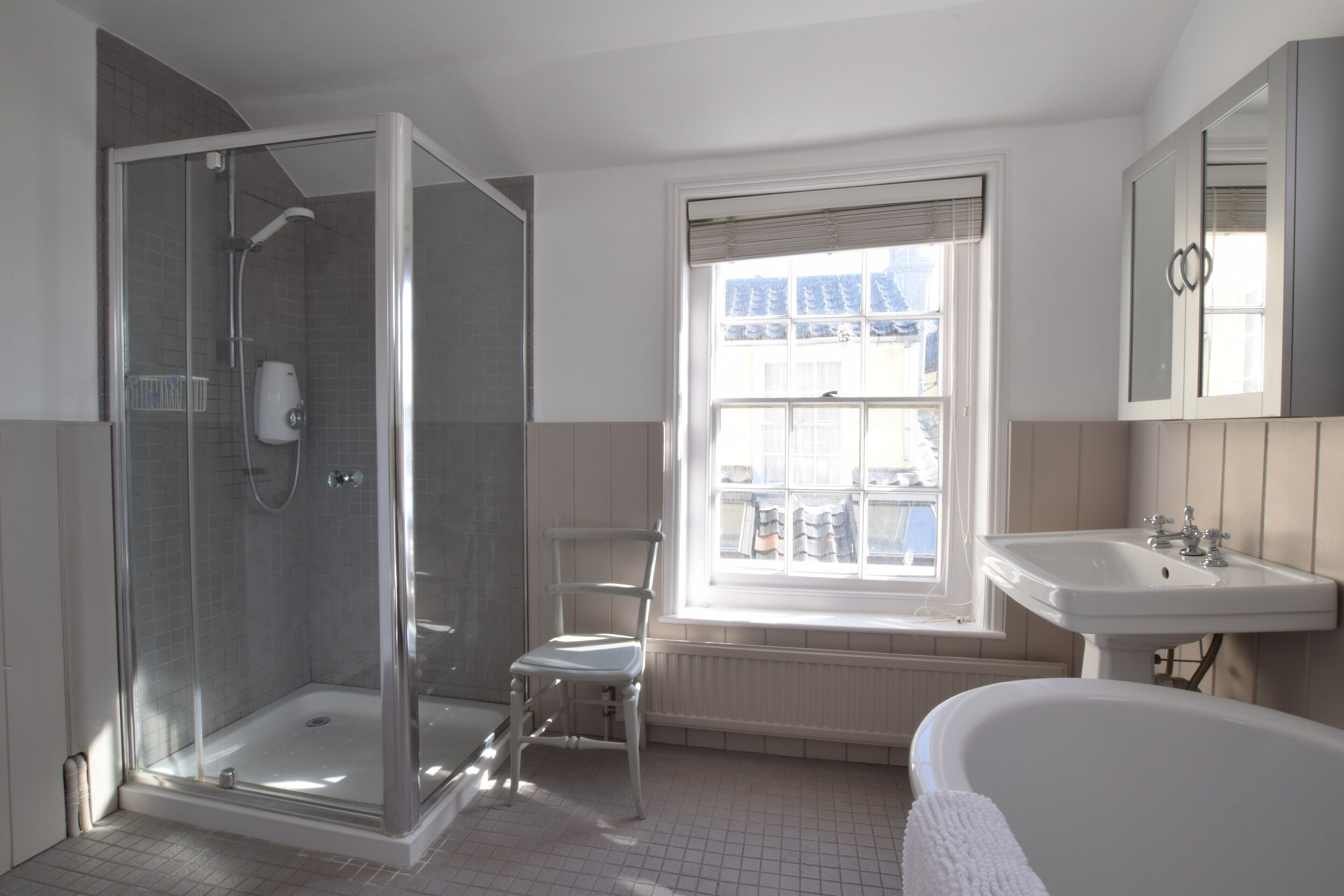 A bathroom with a glass-enclosed shower, a window with blinds, a white sink, and a bathtub.