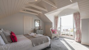Een slaapkamer met een bed, een dressoir, een stoel en een balkon met gordijnen.