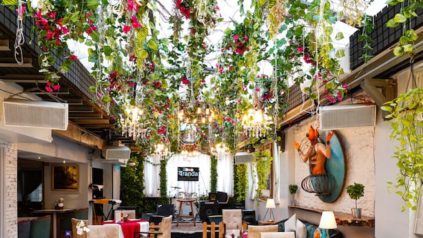 A restaurant with a high ceiling, hanging plants, and a stage for live performances. Tables and chairs are arranged for dining. - Bloom Boutique - Bandra (Mumbai)