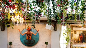 A room with two sofas, a table, and chairs, a painting on the wall, and a decorative ceiling with hanging plants. - Bloom Boutique - Bandra (Mumbai)