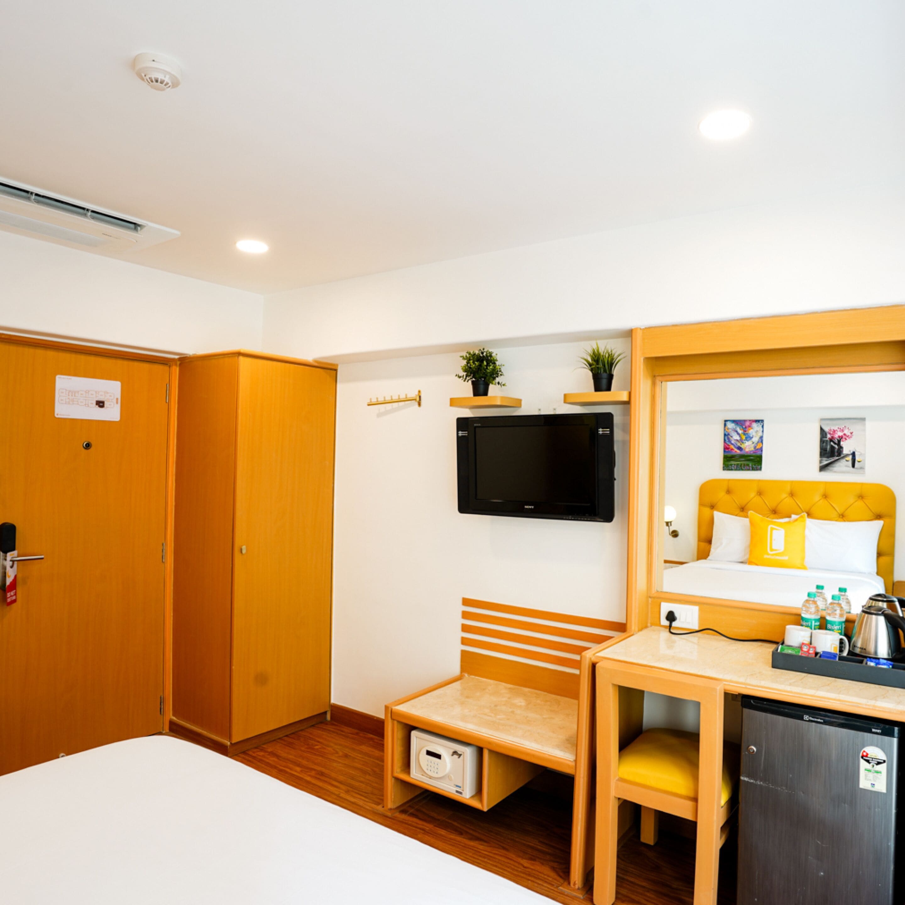 Quarto de hotel com cama, escrivaninha, televisão, micro-ondas, frigorífico e porta com alarme de incêndio.