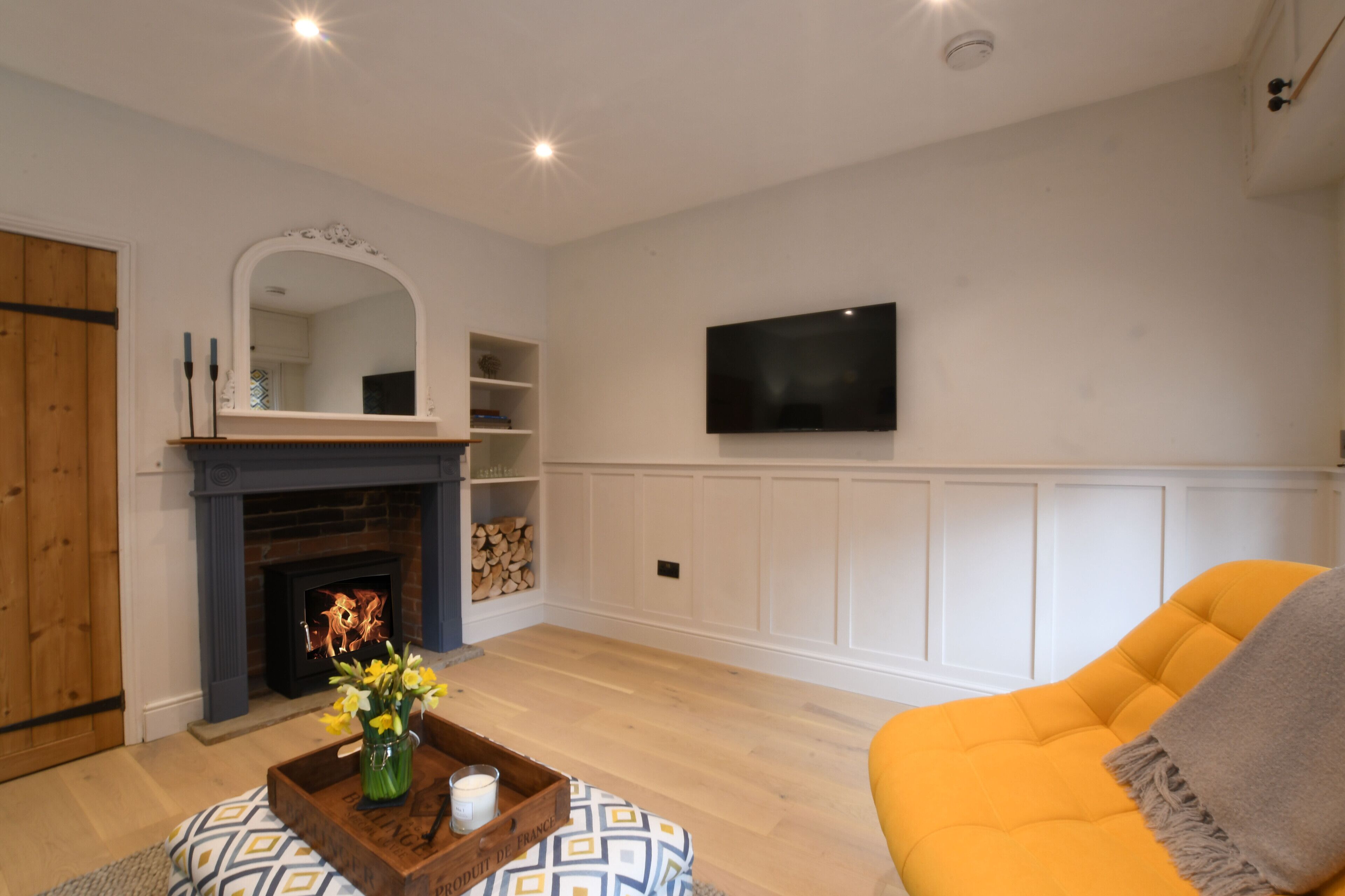 Ein Wohnzimmer mit Kamin, Wand-Fernseher und gelber Couch.