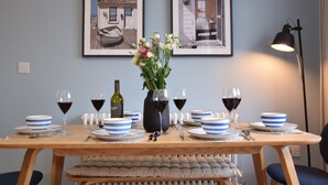 Une table à manger dressée avec des bols à rayures bleues, des verres à vin et un vase rempli de fleurs.