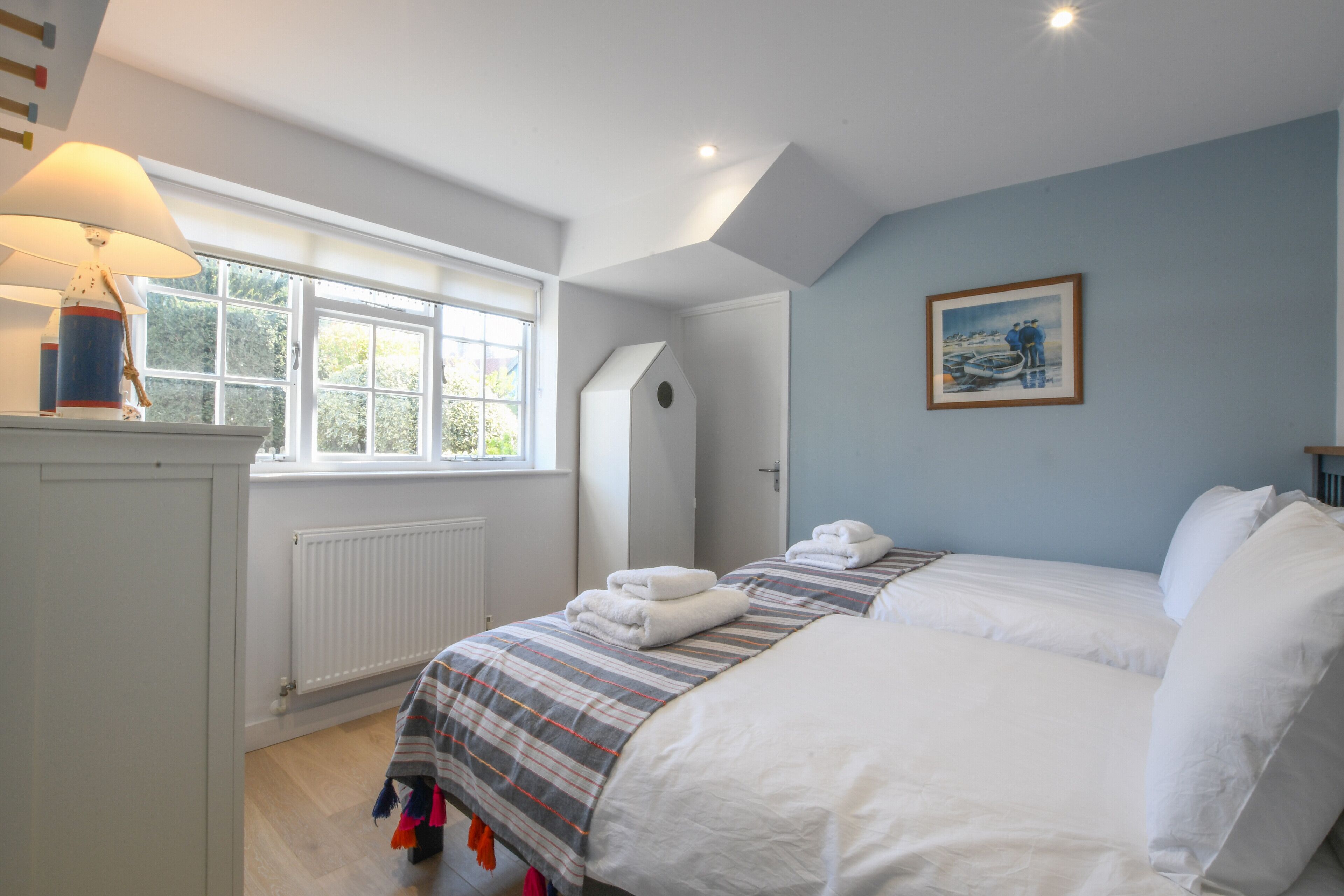 A bedroom with two beds, a window, a radiator, and a painting on the wall.