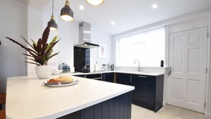 Une cuisine moderne dotée d’un grand îlot central, de meubles de rangement aux couleurs sombres et d’un éclairage suspendu.
