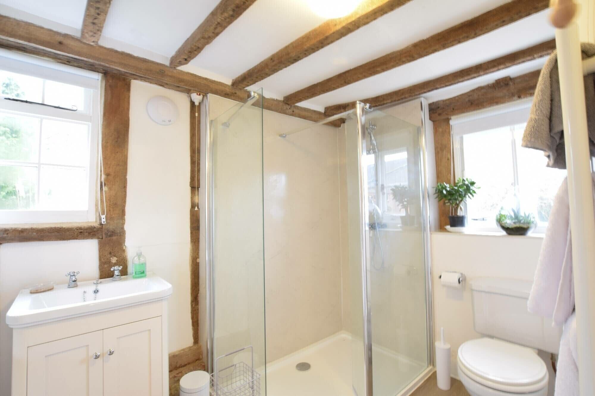 Ein Badezimmer mit Duschkabine aus Glas, einer weißen Toilette und einem Waschbecken mit Spiegel.