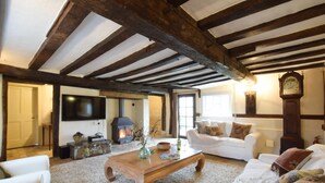 A cozy living room with exposed wooden beams, a fireplace, a white sofa, and a large clock on the wall. - Church Farmhouse, Cookley (Halesworth)