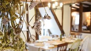 A dining area with a table set for two, wooden chairs, and hanging dried flowers. - Church Farmhouse, Cookley (Halesworth)