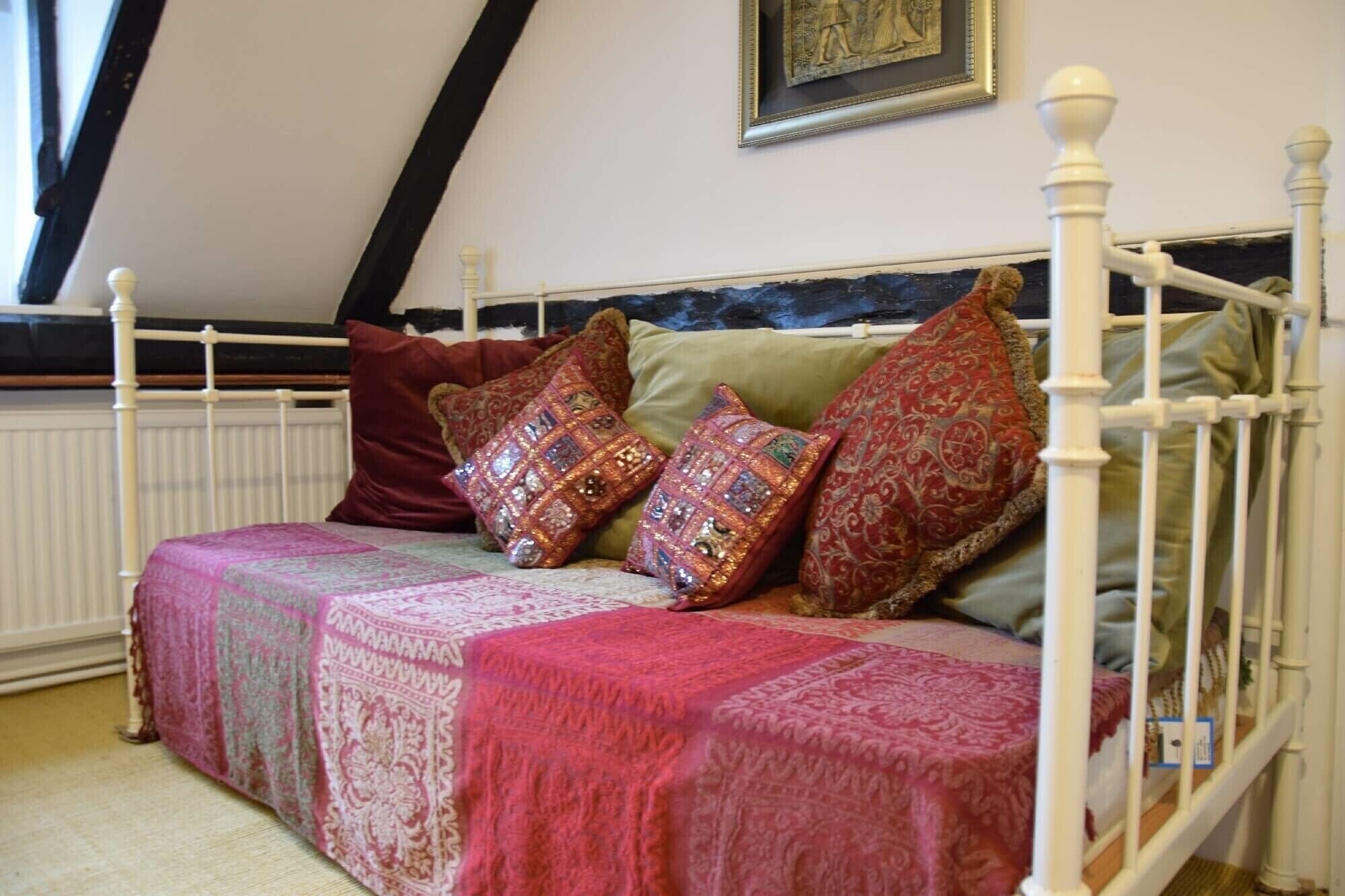 A bed with a patterned bedspread and multiple pillows, a white headboard, and a framed picture on the wall.