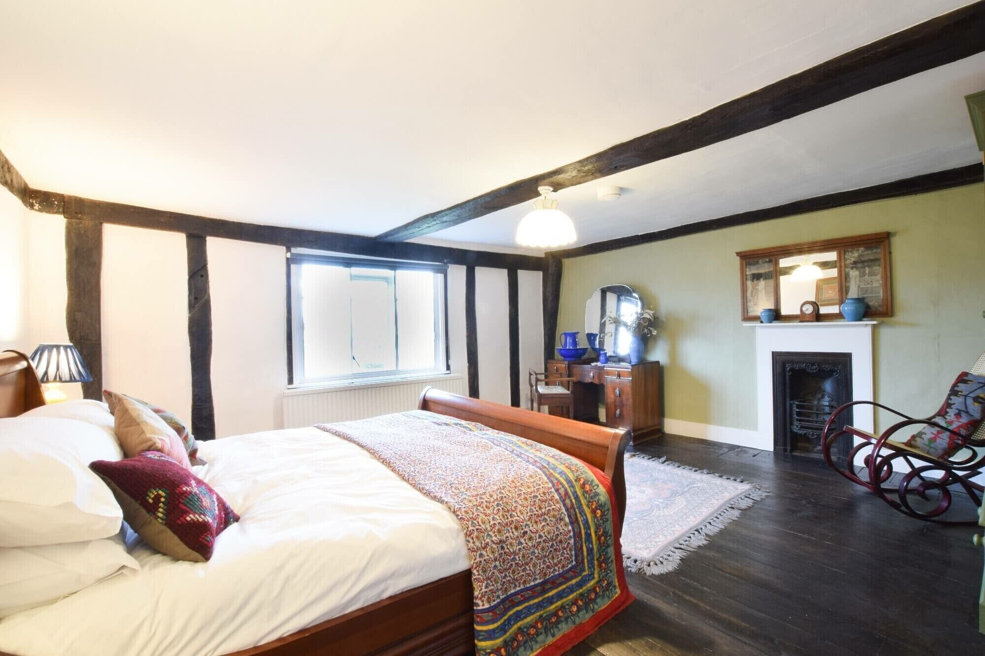 Une chambre à coucher avec un lit, une commode, une chaise, une cheminée et une fenêtre.