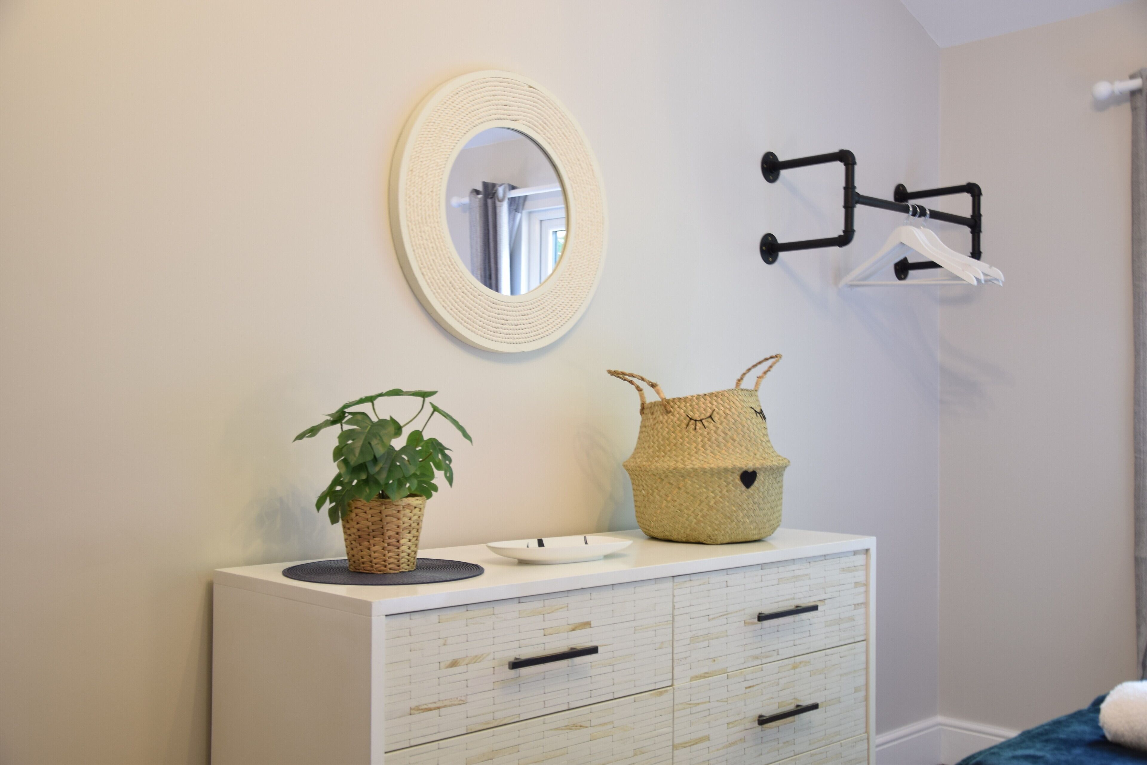 A bathroom with a white vanity, a round mirror, a potted plant, and a woven basket.