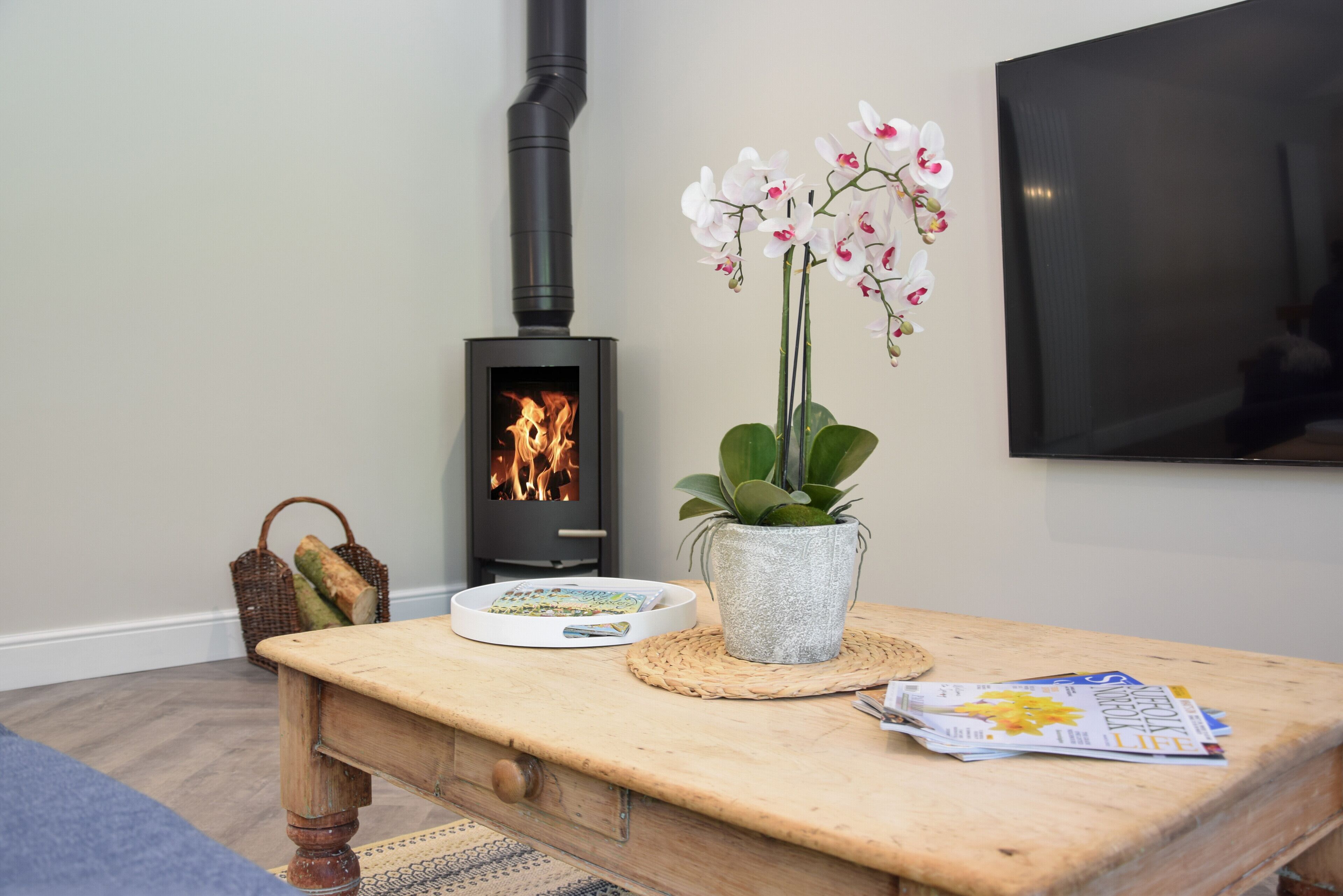 Een gezellige kamer met een houten tafel, een kleine plant in pot, een mand met brood, een tijdschrift en een televisie aan de muur.