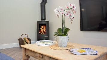 Een gezellige kamer met een houten tafel, een kleine plant in pot, een mand met brood, een tijdschrift en een televisie aan de muur.