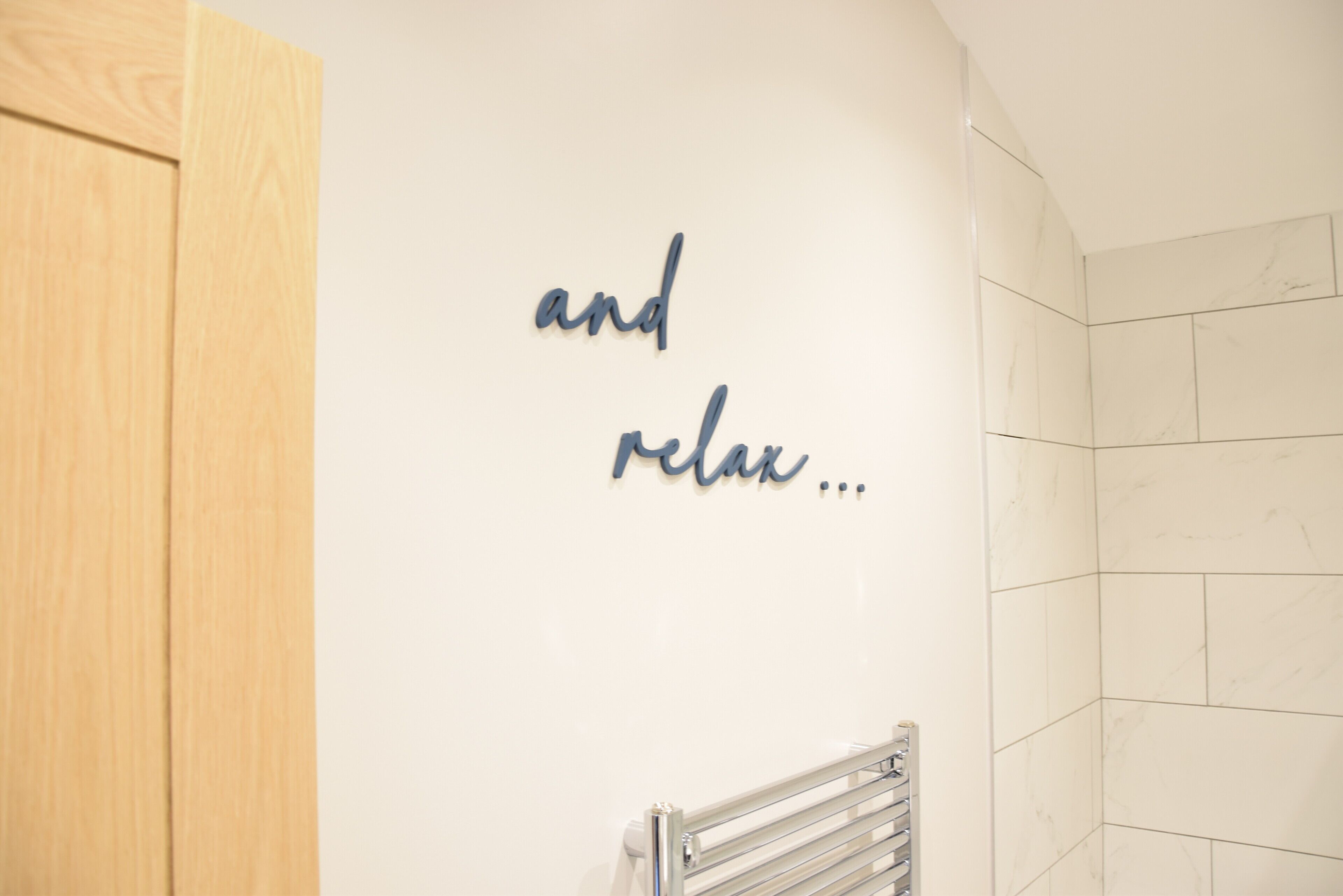 Un baño con puerta de madera, un perchero y una pared con la inscripción 'and relax...'.