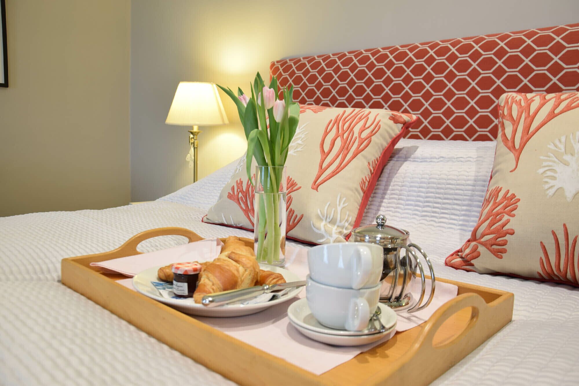 A neatly made bed with a tray of breakfast items including croissants, a cup of coffee, and a glass of water.