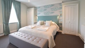 Une chambre à coucher avec un grand lit, deux tables de chevet, un banc et une fenêtre avec des rideaux.