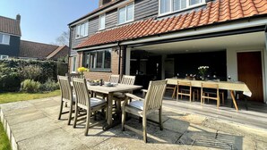 Eine Terrasse mit Esstisch und Stühlen, eine überdachte Außenküche und ein Gartenbereich.