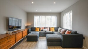 Ein modernes Wohnzimmer mit einer Eckcouch, Hocker, einer Holzkabine und einem Flachbildfernseher.
