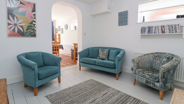 A living room with two teal armchairs, a patterned armchair, a teal sofa, a rug, and a bookshelf with books. - Time Out, Southwold (Reydon)