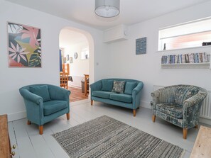 A living room with two teal armchairs, a patterned armchair, a teal sofa, a rug, and a bookshelf with books.