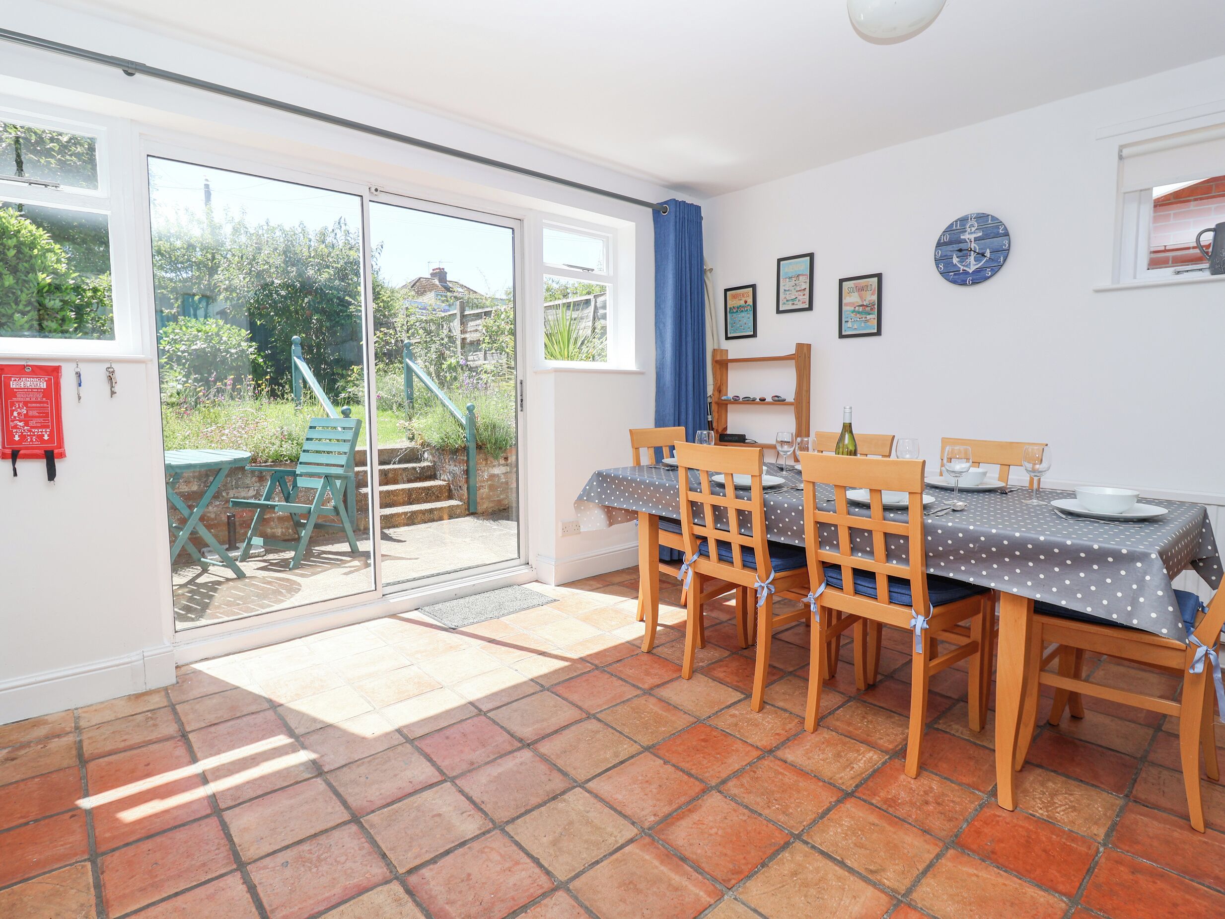 Un comedor con una mesa lista para cuatro personas, sillas de madera, mantel de lunares y vista a un jardín por puertas de cristal.
