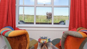 A room with a large window, two colorful chairs, a small table with a mug and a book, and a radiator below. - Time Out, Southwold (Reydon)