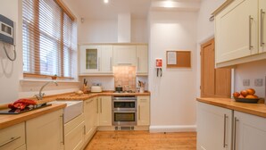 A kitchen with wooden flooring, white cabinets, a built-in oven, and a window with blinds. - 1 Eversley Court, Southwold (Reydon)
