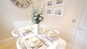 A dining area with a round table set for four, white chairs, a white vase with flowers, and a wall clock.