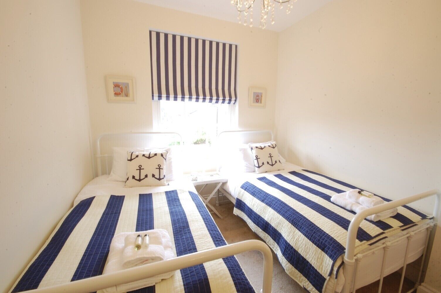 Ein Zimmer mit zwei Betten, jeweils mit gestreifter Bettwäsche und passenden Kissen, einem Fenster mit einem Streifenrollo und einem kleinen Tisch zwischen den Betten.