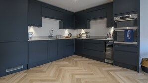 Una cocina moderna con armarios oscuros, piso de madera en espiga y electrodomésticos integrados.