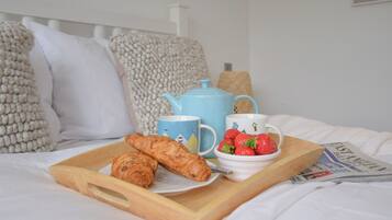 Bandeja de desayuno con cruasanes, un hervidor, una taza y un bol de fresas sobre una mesita.
