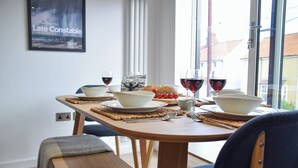 Un área de comedor con una mesa de madera dispuesta para dos personas, incluyendo cuencos, platos y copas de vino tinto.