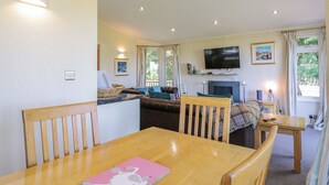 A cozy living room with a wooden dining table, a sofa, and a television mounted on the wall. - The Hide Out, Aldeburgh (Aldeburgh)