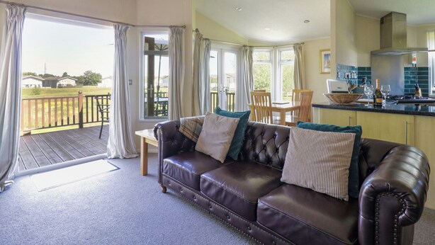 A living room with a leather sofa, dining table, and chairs. There is a kitchen area with a stove and cabinets. A balcony with a railing is visible. - The Hide Out, Aldeburgh (Aldeburgh)