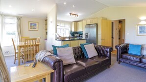 A spacious living room with a brown leather sofa, a wooden dining table, and a kitchen in the background. - The Hide Out, Aldeburgh (Aldeburgh)