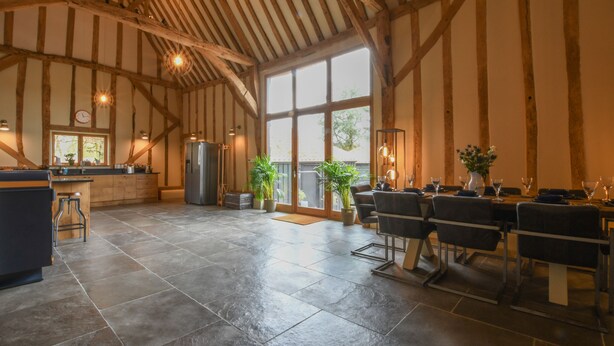 A spacious kitchen with a large island, wooden beams, and a dining area with a table set for six. - Halcyon Barn, Wissett (Halesworth)