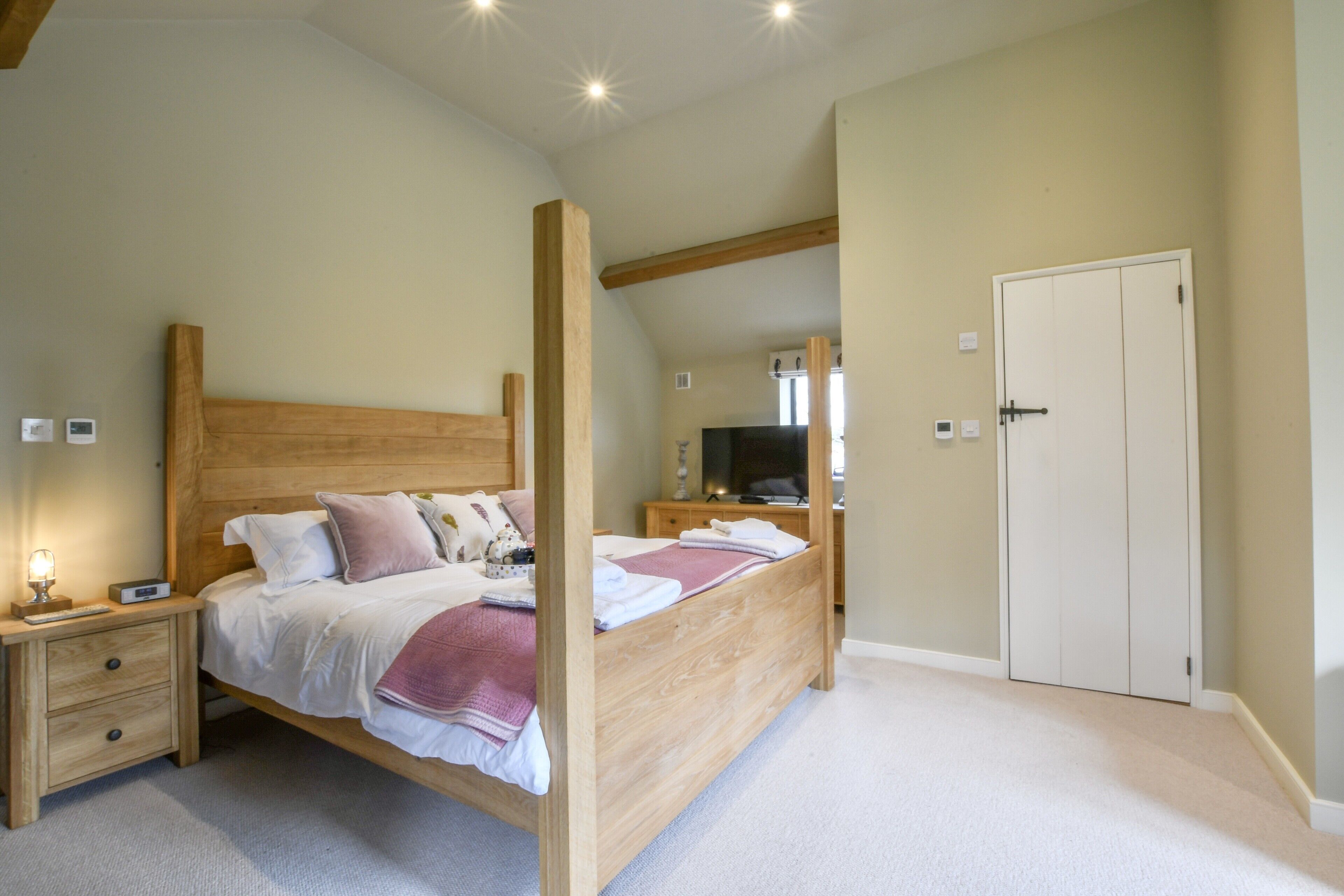 Une chambre à coucher avec un lit à baldaquin en bois, une table de chevet avec une lampe, une armoire et un téléviseur en arrière-plan.