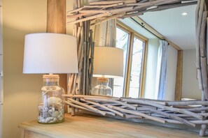 A room with a wooden table, a glass bottle with seashells, and a mirror with wooden branches. - Halcyon Barn, Wissett (Halesworth)