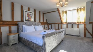 Una camera da letto con un letto grande, travi in legno, un comodino, un termosifone e una finestra con tende.
