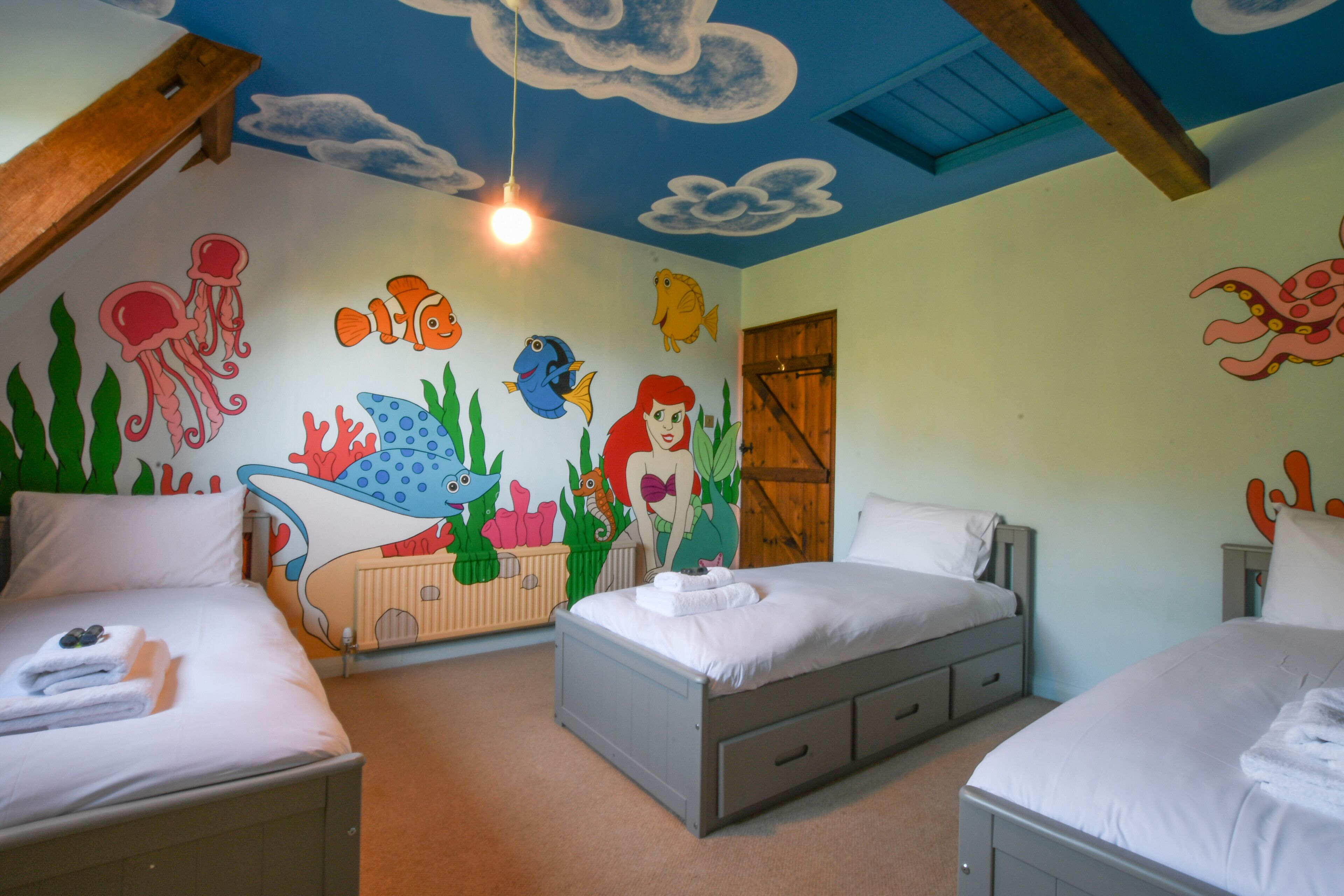 Una stanza con due letti, un affresco con creature marine e una trave in legno al soffitto.