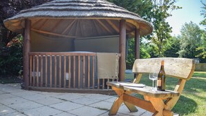 Un gazebo in legno con tetto di paglia, un tavolo da picnic e una bottiglia di vino.