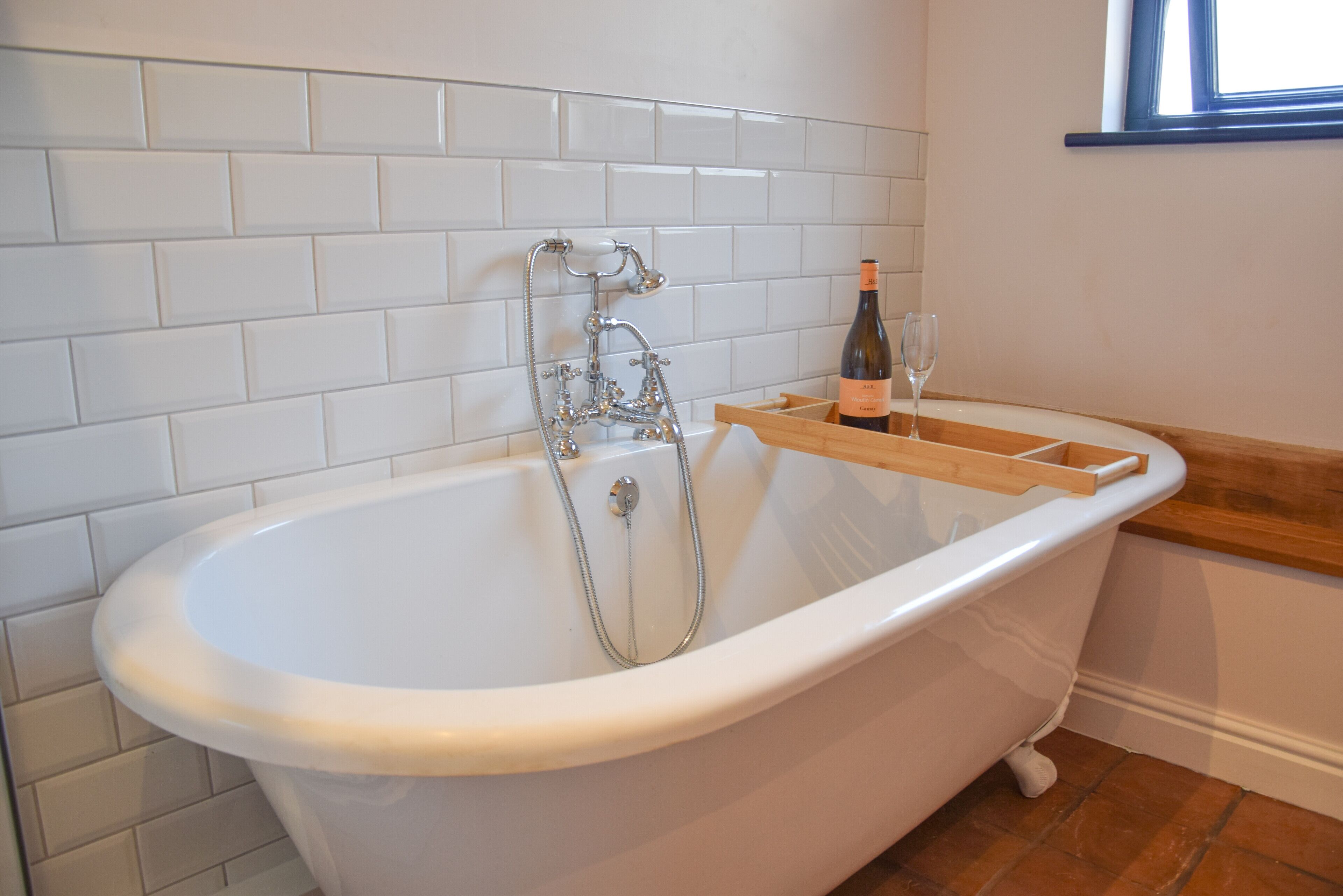 Eine weiße, freistehende Badewanne mit einem hölzernen Tablett, einer Weinflasche und einem Glas daneben.