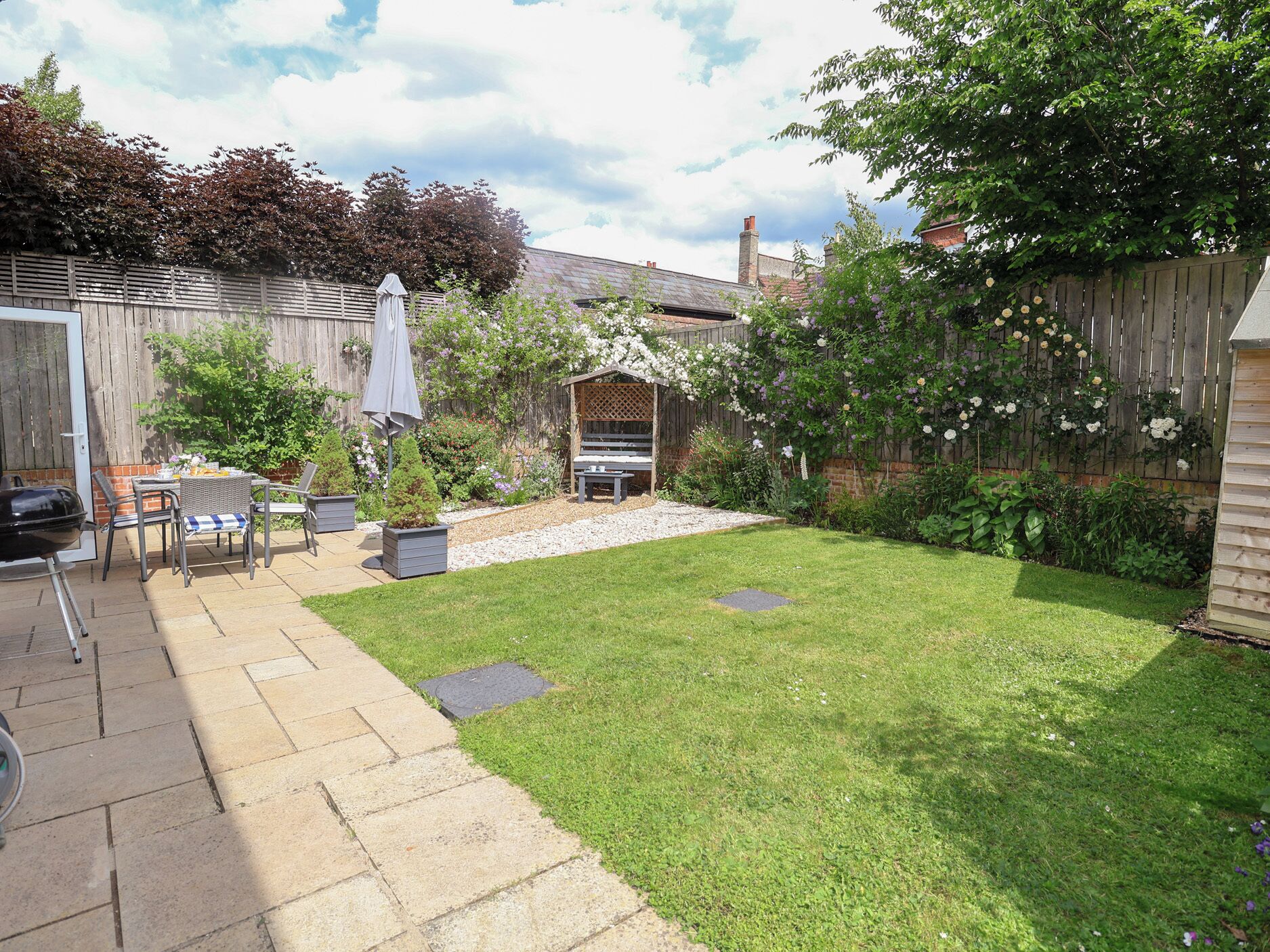 A backyard with a patio area, a wooden fence, and a garden with various plants and flowers.