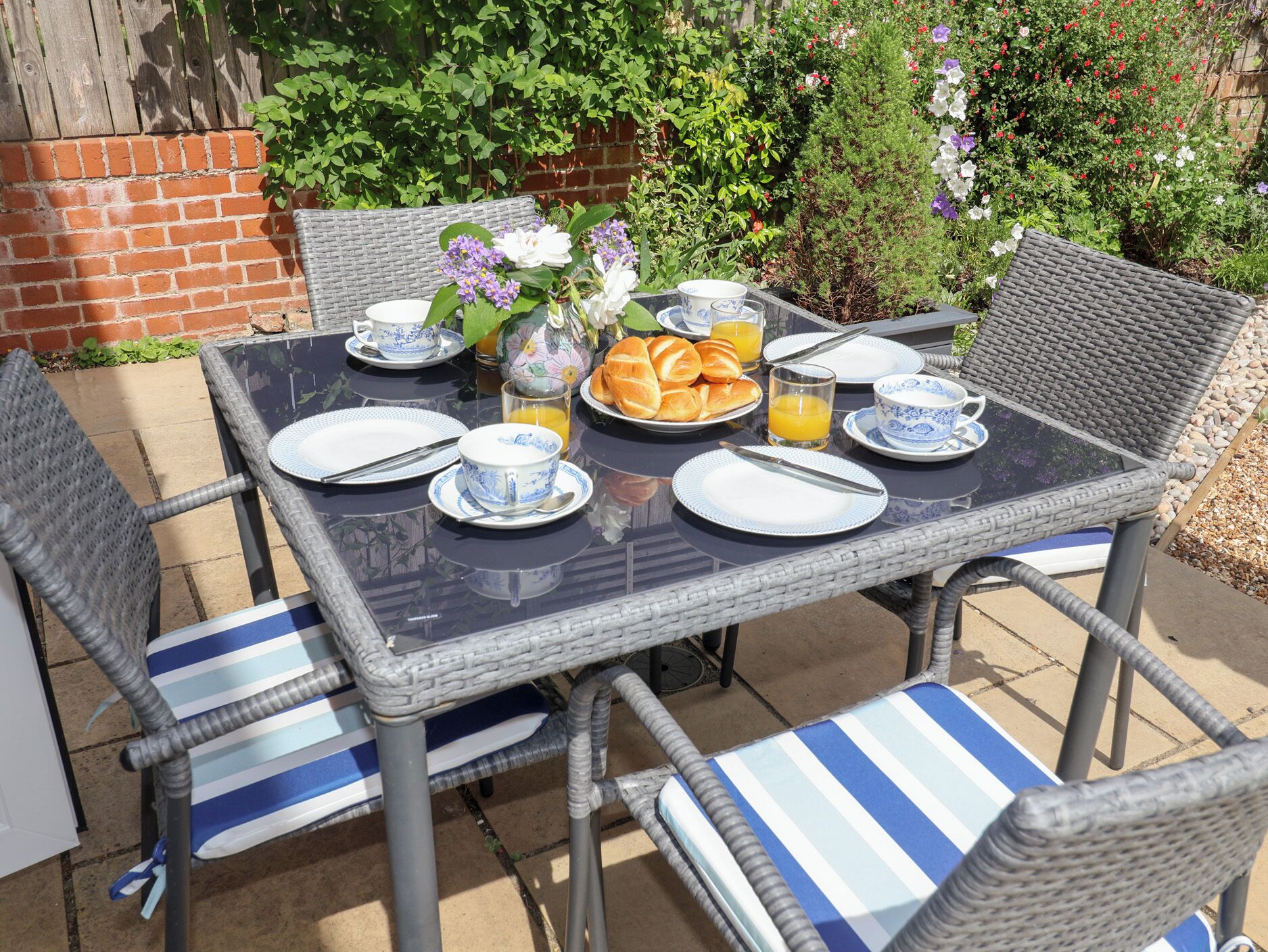 An outdoor dining area with wicker chairs and a glass table set for breakfast.