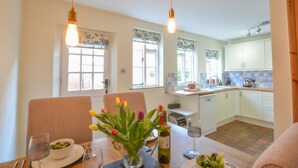 Un coin repas avec une table dressée pour deux personnes, un vase de tulipes et une bouteille de vin.