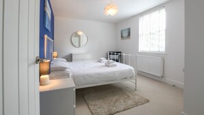 A bedroom with a bed, bedside lamps, a round mirror, a radiator, and a window. - The Gallery, Blythburgh (Halesworth)